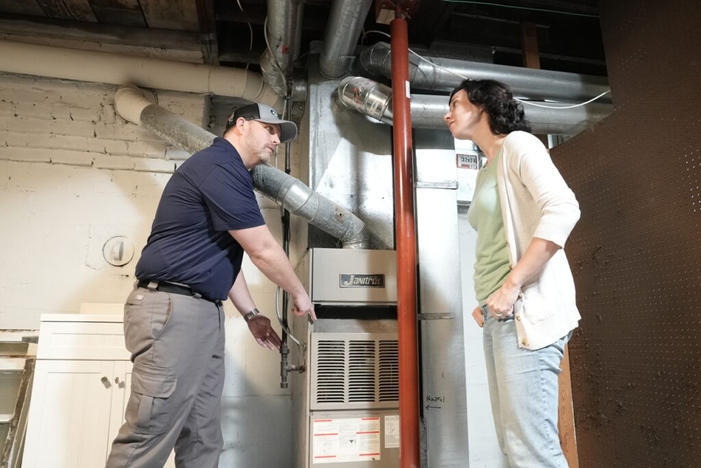 HVAC technician and homeowner looking at a furnace